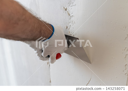 Technician applying finishing plaster using stainless steel trowel on wall surface. Clean working area with smooth drywall texture visible in background. Technician applying finishing plaster using stainless steel trowel on wall surface. Clean working area with smooth drywall texture visible in background. 143258071