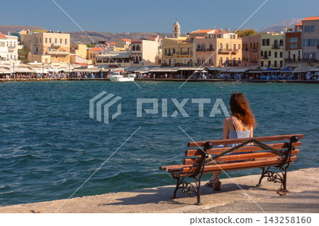 Title EN: Woman sitting by the Old Venetian Harbor in Chania, Crete, Greece 143258160