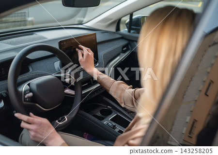 A driver interacts with a high tech touchscreen display while seated in a contemporary electric vehicle. A driver interacts with a high tech touchscreen display while seated in a contemporary electric vehicle. 143258205
