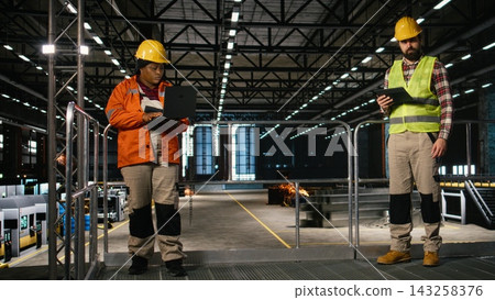 Mechanical expert, reviewing heavy equipment, performance on tablet, busy factory interior. Massive machinery and steel work dominate the industry hall and support large-scale production. Mechanical expert, reviewing heavy equipment, performance on tablet, busy factory interior. Massive machinery and steel work dominate the industry hall and support large-scale production. 143258376