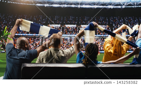 Soccer supporters waving scarves during football game in living room as immersive TV broadcast makes them feel closer to stadium pitch. Football fans doing loud chant, feeling crowd energy 143258382