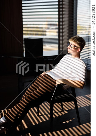 Casual student rests with thoughtful demeanor near window Casual student rests with thoughtful demeanor near window 143258921
