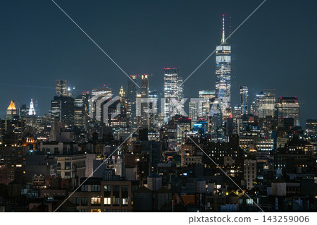 New York Financial District skyline at night with One World Trade Center rising above modern skyscrapers. The illuminated downtown buildings create a dramatic urban cityscape with glowing office New York Financial District skyline at night with One World Trade Center rising above modern skyscrapers. The illuminated downtown buildings create a dramatic urban cityscape with glowing office 143259006