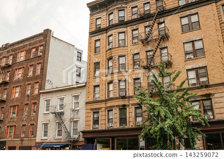 Classic Manhattan brick apartment buildings with black metal fire escapes and rows of windows along a city street. Historic New York residential architecture featuring vintage facade design and urban Classic Manhattan brick apartment buildings with black metal fire escapes and rows of windows along a city street. Historic New York residential architecture featuring vintage facade design and urban 143259072