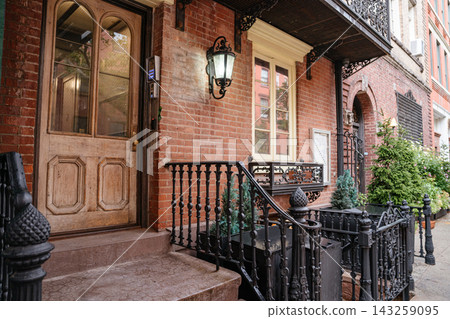 Traditional New York brownstone entrance with wooden door, iron railing, and brick facade along a quiet residential street. Historic Manhattan architecture featuring detailed exterior design and urban Traditional New York brownstone entrance with wooden door, iron railing, and brick facade along a quiet residential street. Historic Manhattan architecture featuring detailed exterior design and urban 143259095