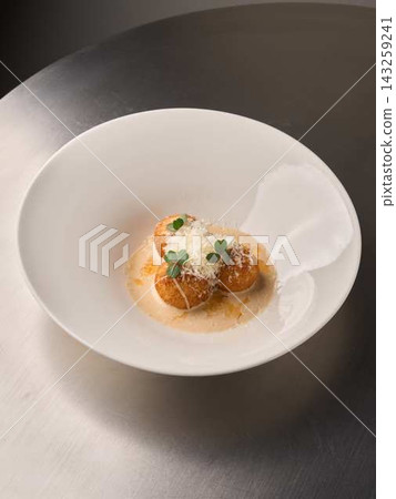 Crispy golden croquettes served in white bowl with velvety cream sauce, microgreens, and parmesan shavings on reflective stainless steel tabletop, gourmet appetizer Crispy golden croquettes served in white bowl with velvety cream sauce, microgreens, and parmesan shavings on reflective stainless steel tabletop, gourmet appetizer 143259241