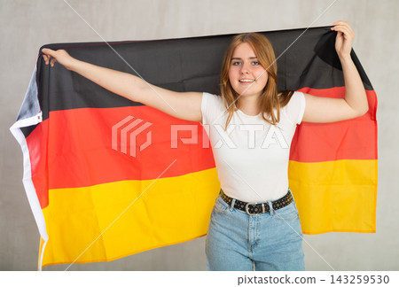 smiling girl in arms raised above head holds canvas of national flag of Germany 143259530