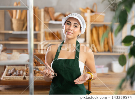 Young woman seller with tongs in bakery Young woman seller with tongs in bakery 143259574