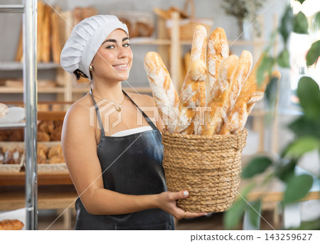 Young saleswoman displays baguettes in wicker basket Young saleswoman displays baguettes in wicker basket 143259627