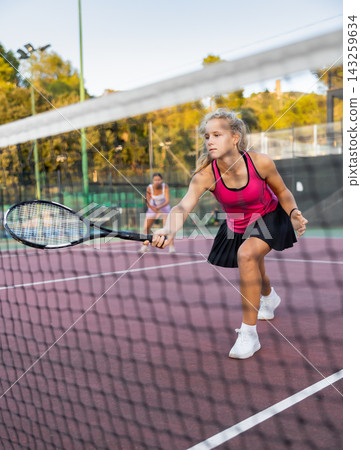 Sportive woman in shorts and t-shirt playing tennis on court. View through tennis net Sportive woman in shorts and t-shirt playing tennis on court. View through tennis net 143259634