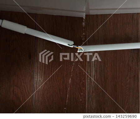 Heavy storm rain create water flow from edge of ceiling. Water leaking from top ceiling as droplets and flow in old house with broken electric wire pipe white tube for power supply cable Heavy storm rain create water flow from edge of ceiling. Water leaking from top ceiling as droplets and flow in old house with broken electric wire pipe white tube for power supply cable 143259690