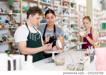 Female potter teaches guy how to apply design and glaze on pottery Female potter teaches guy how to apply design and glaze on pottery 143259706