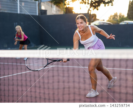 Positive female player hits ball close to net while playing tennis Positive female player hits ball close to net while playing tennis 143259734