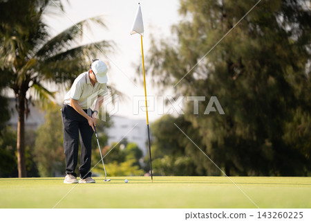 Male golfer kneeling on green reading putting line before stroke Male golfer kneeling on green reading putting line before stroke 143260225