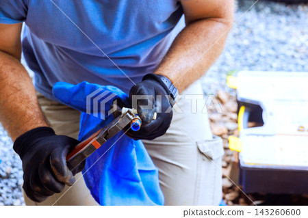 Worker is in yard working with tools he holds water pipes with pliers uses cloth to wipe it. 143260600