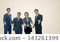 Four businessmen, two men and two women, extend their hands with smiles against a beige background with a large margin on the right. 143261399