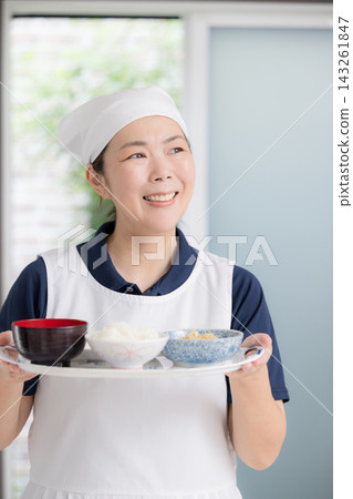 一位面帶微笑的女工作人員正在老人家中準備餐點；家事服務、烹飪協助、居家照護、膳食支援、送餐服務圖片。 143261847