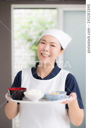 Smiling female staff preparing meals in the homes of elderly people; housekeeping, cooking assistance, home care, meal support, meal service image. Smiling female staff preparing meals in the homes of elderly people; housekeeping, cooking assistance, home care, meal support, meal service image. 143261848