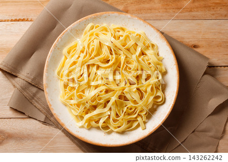 Cooked fresh fettuccine served on a rustic wooden plate with a cloth napkin. 143262242