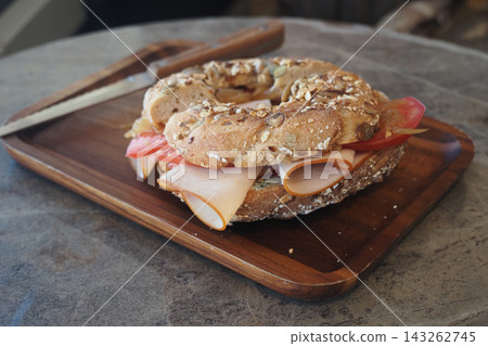 Fresh bagel with ham and tomato on a wooden tray in a cafe Fresh bagel with ham and tomato on a wooden tray in a cafe 143262745