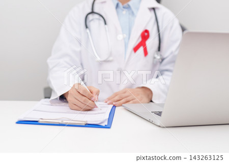 doctor using laptop and report notes on notebook. red ribbon concept of December World Aids Day, MADD, October Red ribbon week, February Heart month, Marfan Syndrome, May Stroke awareness doctor using laptop and report notes on notebook. red ribbon concept of December World Aids Day, MADD, October Red ribbon week, February Heart month, Marfan Syndrome, May Stroke awareness 143263125