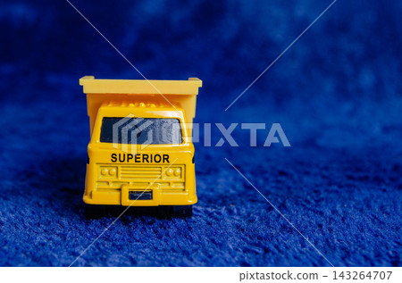 Small yellow toy truck placed on a blue surface with the word superior printed on the side Small yellow toy truck placed on a blue surface with the word superior printed on the side 143264707