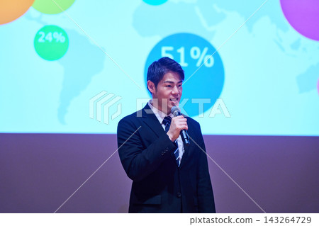 A Japanese man gives a presentation with a microphone in front of a screen. A Japanese man gives a presentation with a microphone in front of a screen. 143264729