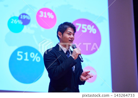 A Japanese man gives a presentation with a microphone in front of a screen. A Japanese man gives a presentation with a microphone in front of a screen. 143264733