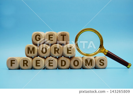 Get More Freedoms alphabet letters wooden cube and magnifying glass on blue background Get More Freedoms alphabet letters wooden cube and magnifying glass on blue background 143265809