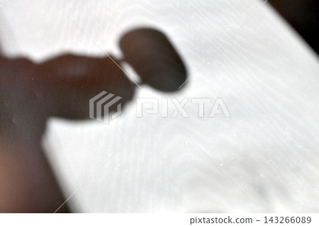 A blurred hand shadow on a light, textured background. A blurred hand shadow on a light, textured background. 143266089