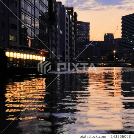 夕陽西下，一艘船屋沿著中之島的堂島川緩緩駛向難波大橋。 （方形圖片） 143266098
