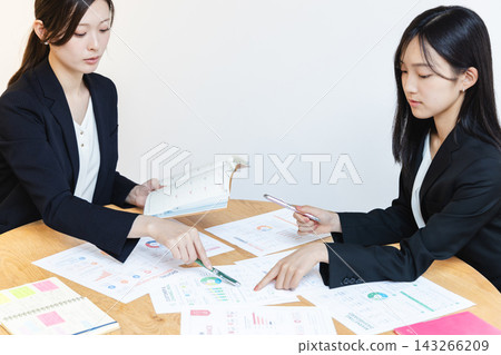 兩名女員工認真地分析數據並核對日程安排,同時指著文件。 兩名女員工認真地分析數據並核對日程安排,同時指著文件。 143266209