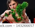 Woman Decorating a Small Christmas Tree with Tinsel and Baubles 143266657