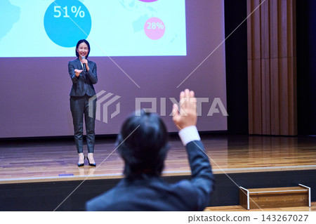 A female presenter responding to a participant who raised their hand at the presentation venue. A female presenter responding to a participant who raised their hand at the presentation venue. 143267027