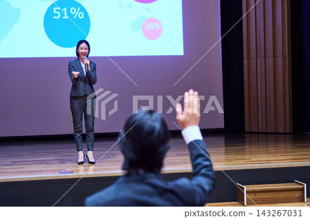 A female presenter responding to a participant who raised their hand at the presentation venue. A female presenter responding to a participant who raised their hand at the presentation venue. 143267031