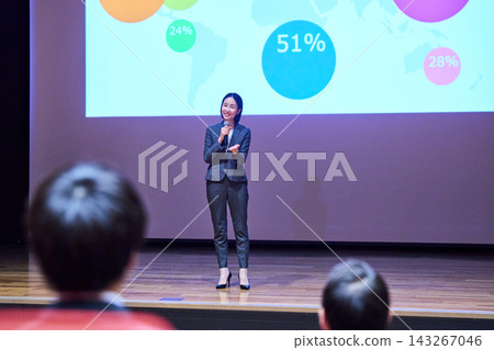 一位女士正在用麥克風做演講,她身後是一塊螢幕。 一位女士正在用麥克風做演講,她身後是一塊螢幕。 143267046