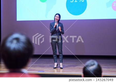 一位女士正在用麥克風做演講,她身後是一塊螢幕。 一位女士正在用麥克風做演講,她身後是一塊螢幕。 143267049