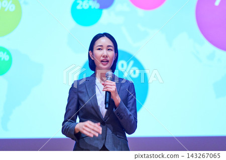 一位女商人正在用麥克風做演講，她身後有一個螢幕。 143267065