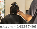 Professional hairstylist using electric hair clippers to trim and shape a client in hair salon. 143267496