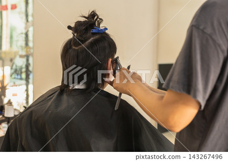 Professional hairstylist using electric hair clippers to trim and shape a client in hair salon. Professional hairstylist using electric hair clippers to trim and shape a client in hair salon. 143267496