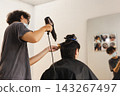 Professional male hairstylist blow drying client's hair in hair salon. 143267497