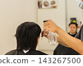 Hairstylist spraying water onto a client's hair using a spray bottle  in salon setting. 143267500