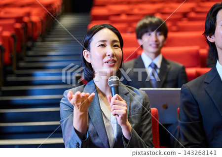 A woman in a suit opens her laptop and gives her opinion at a business event. A woman in a suit opens her laptop and gives her opinion at a business event. 143268141