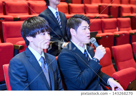 一位身穿西裝的男士與其他聽眾一起，在講座現場積極提問。 143268270