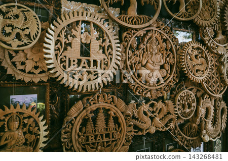 Balinese wood carvings and handmade wall decor displayed in Bali artisan market. Traditional Indonesian craftsmanship, boho interior design and cultural travel concept Balinese wood carvings and handmade wall decor displayed in Bali artisan market. Traditional Indonesian craftsmanship, boho interior design and cultural travel concept 143268481