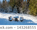 Wooden table and bench covered with snow in a peaceful winter landscape, creating a simple and atmospheric outdoor scene. 143268555