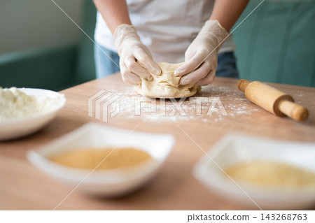 Woman in gloves kneading fresh dough on a wooden table Woman in gloves kneading fresh dough on a wooden table 143268763