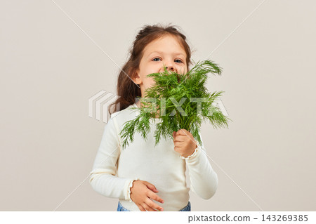 Young child holding a bunch of green dill, peeking out, promoting healthy eating and fresh organic vegetables Young child holding a bunch of green dill, peeking out, promoting healthy eating and fresh organic vegetables 143269385