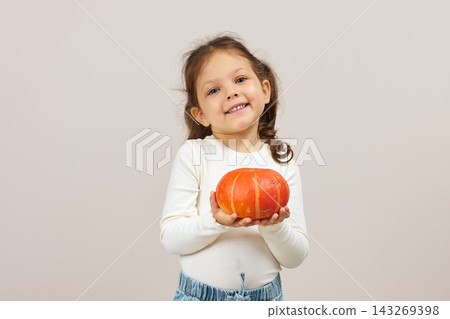 Happy child in a studio portrait posing with an orange pumpkin, celebrating harvest, halloween, and fall season Happy child in a studio portrait posing with an orange pumpkin, celebrating harvest, halloween, and fall season 143269398