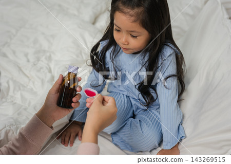 mother feeding liquid medicine to sick preschool child girl with a spoon mother feeding liquid medicine to sick preschool child girl with a spoon 143269515